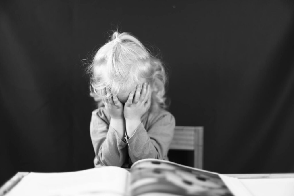 child with blonde hair covering face with hands